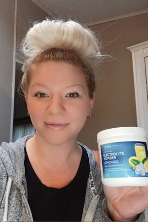 A woman with Dr. Berg Electrolyte Powder Lemonade Flavor product
