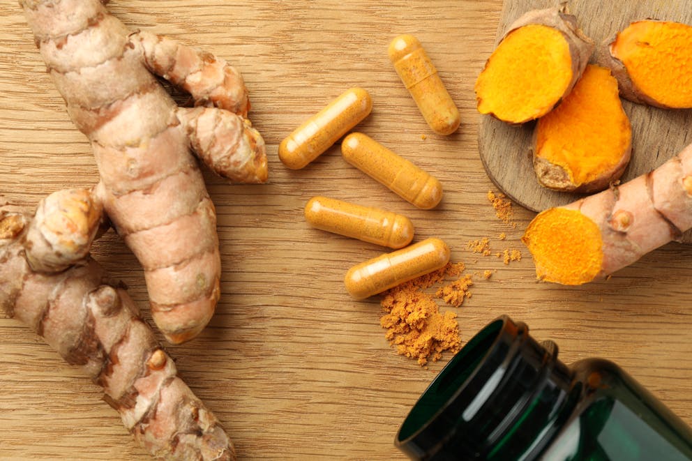Turmeric powder, raw roots, and pills on a wooden table