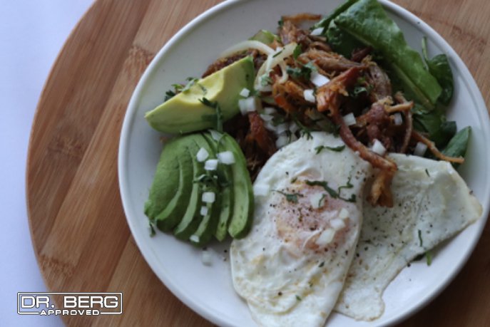 Breakfast plate with two fried eggs, pulled pork, greens, and avocado