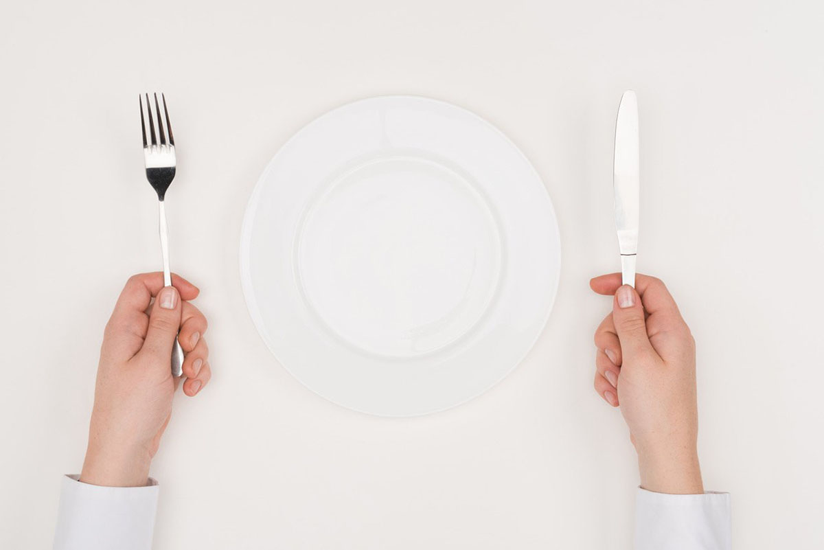 Person holding fork and knife in each hand with an empty plate on the table