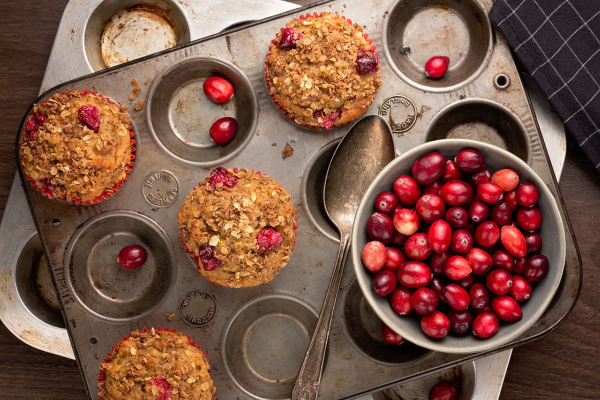 Freshly baked cranberry pecan muffins coming out of the tin with a bowl of cranberries