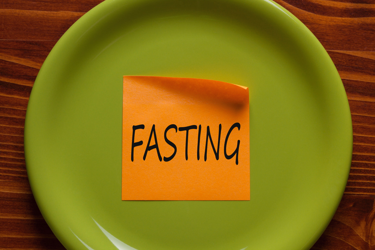 FASTING written on an orange sticky note on top of an empty green plate.
