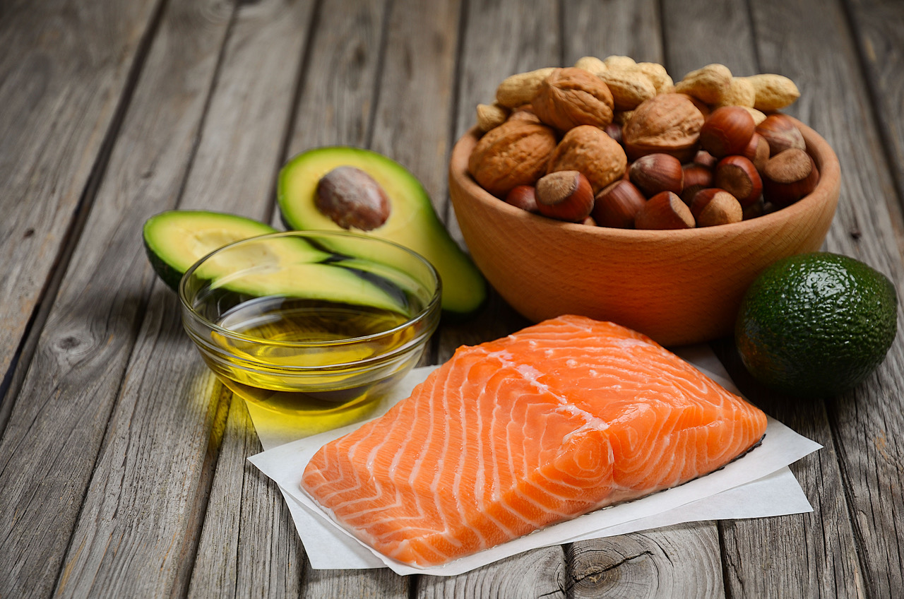 A selection of healthy fat sources like salmon, nuts, olive oil, and avocados