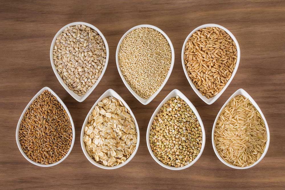 Assorted whole grains in bowls on a wood table.