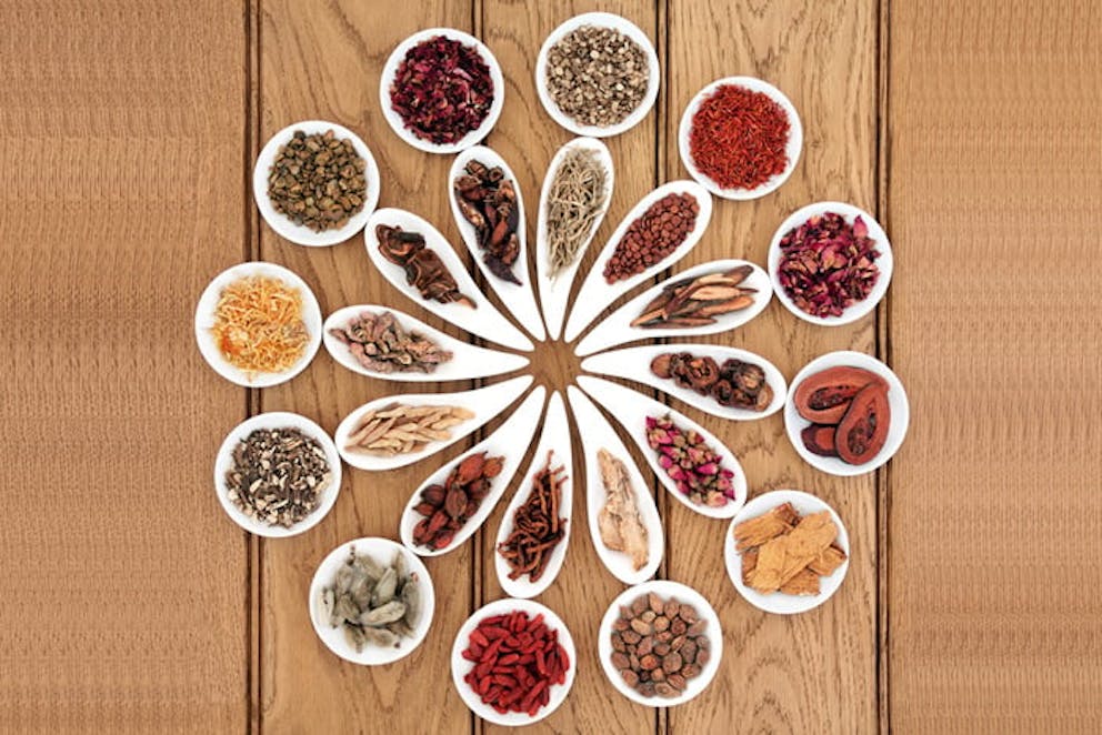 Traditional Chinese medicine herbal remedies in white dishes, arranged in shape of flower on table.