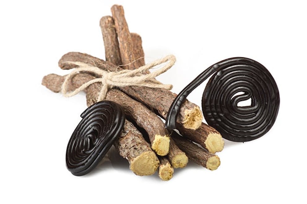 Licorice root herbal remedy tied with twine next to black licorice swirls on white background.