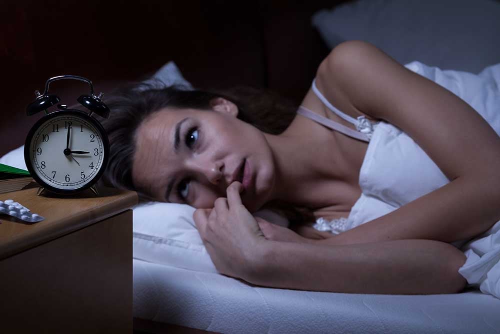 woman lying in bed staring at the clock | 7 Foods That Help You Sleep Better