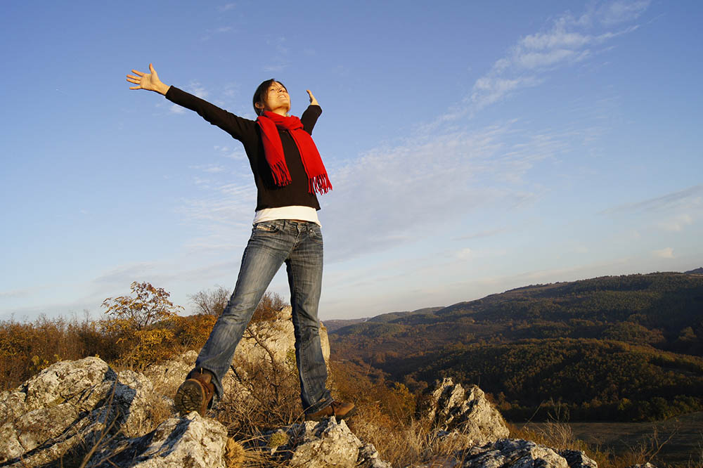 energetic woman standing on rocks celebrating her success