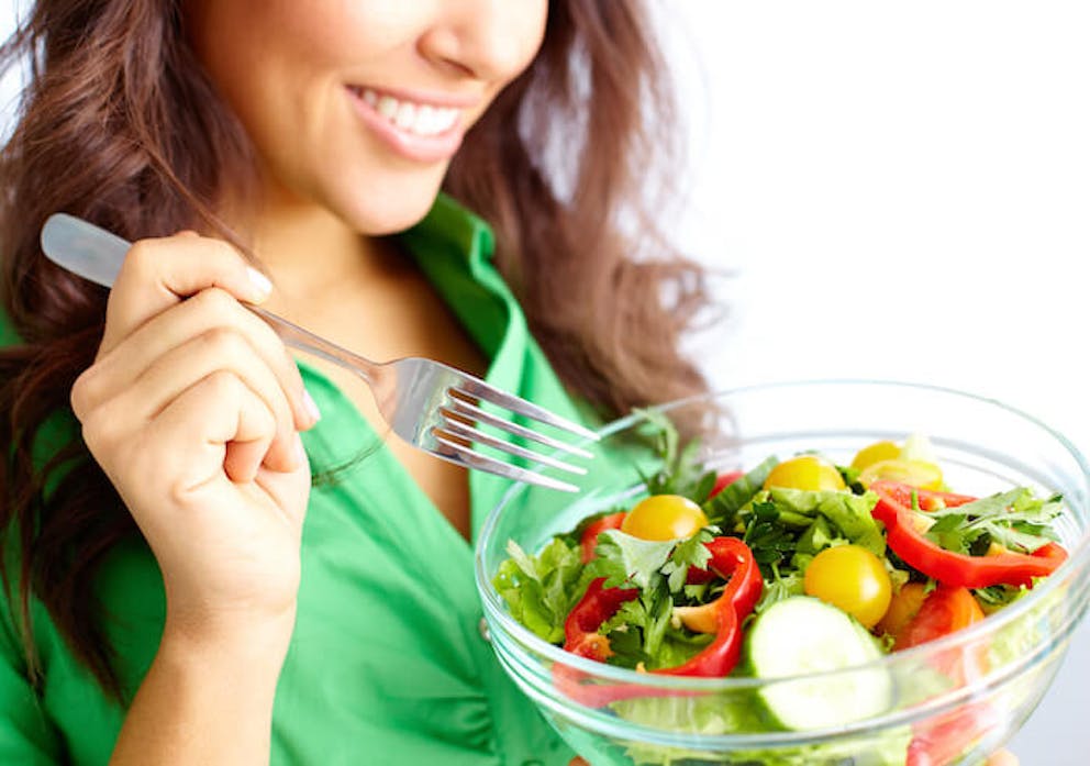 A close-up of a pretty woman smiling and eating a large healthy salad. | 7 Things that Boost Fat Storing Hormone Sensitivity or Reverse Fat Storing Hormone Resistance