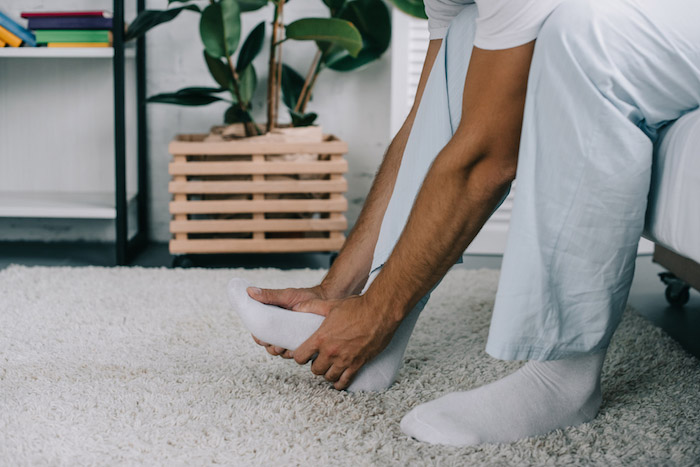 Man getting out of bed and holding foot in pain. |  7 Tips to Lower Uric Acid