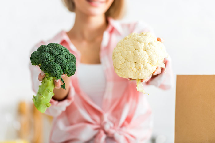 Woman holding up a head of broccoli and a head of cauliflower |  7 Tips to Lower Uric Acid