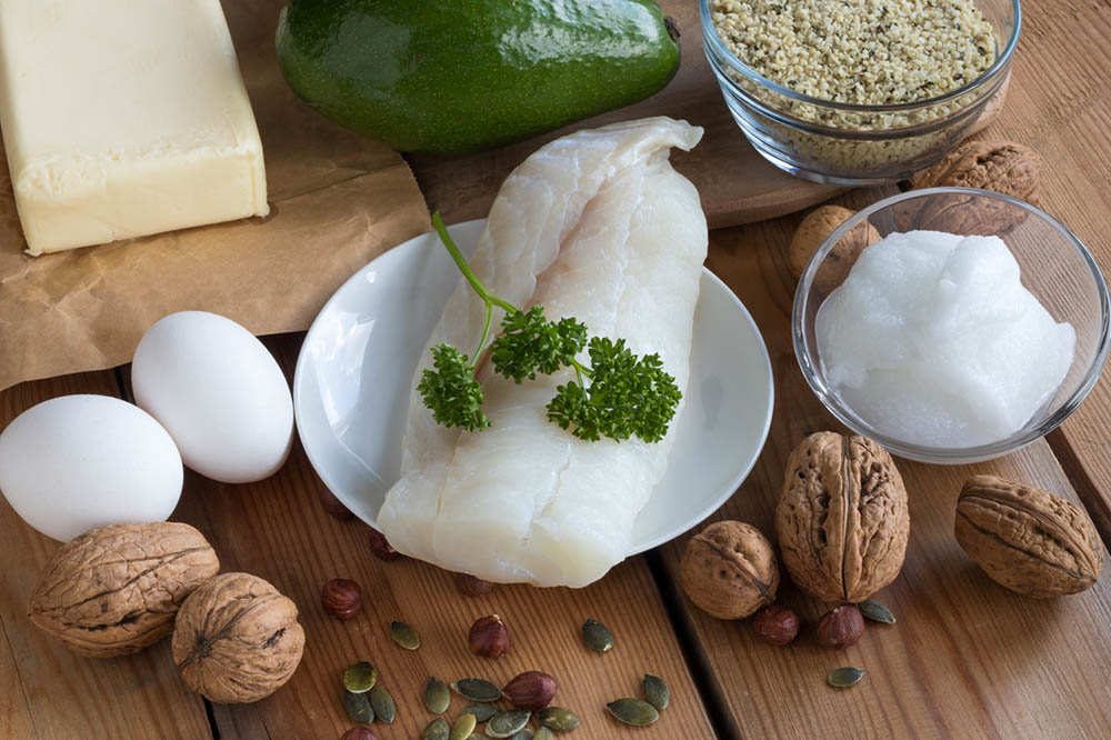 A selection of healthy fats for the keto diet like fish, nuts, eggs, butter, and coconut oil.