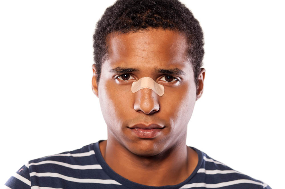 A man in a striped shirt with a bandage over his nose injury.