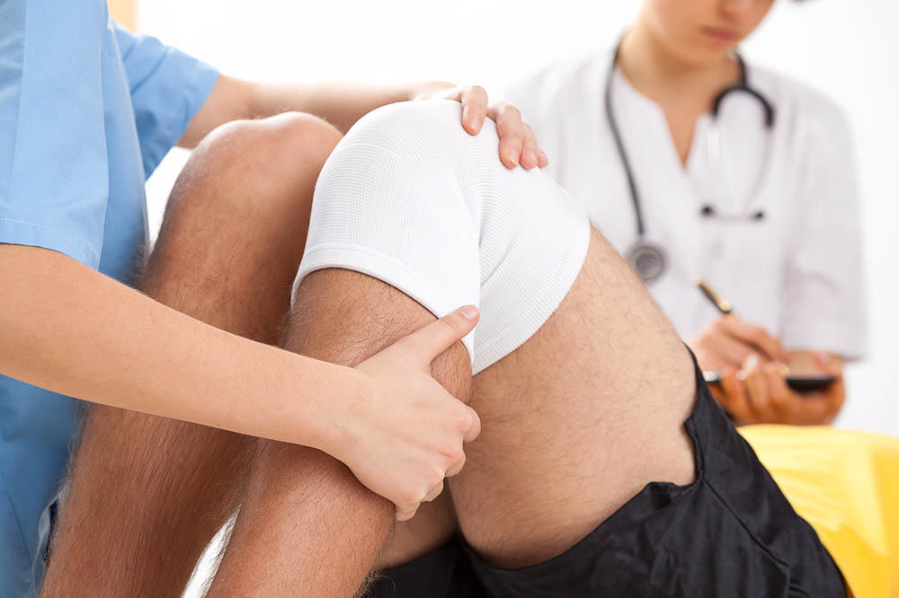 Doctors work on bandaged knee of a man recovering from knee surgery | acupressure post-surgery pain