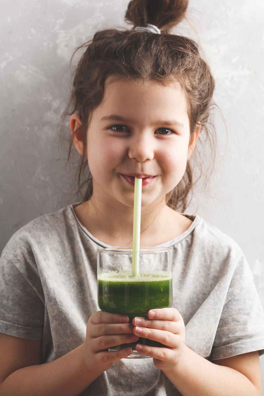 A happy young girl drinking a healthy green kale shake and smiling