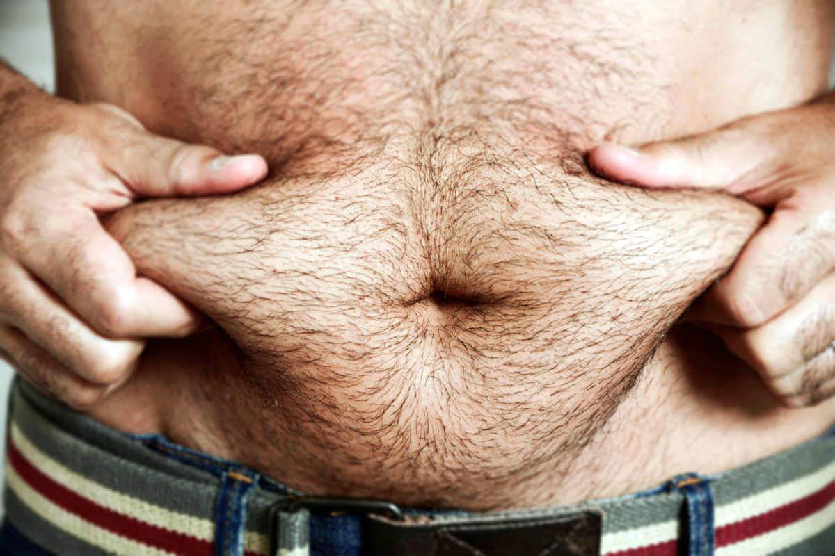 Closeup of a young caucasian man grabbing the fat of his hairy stomach | Adrenal Fatigue