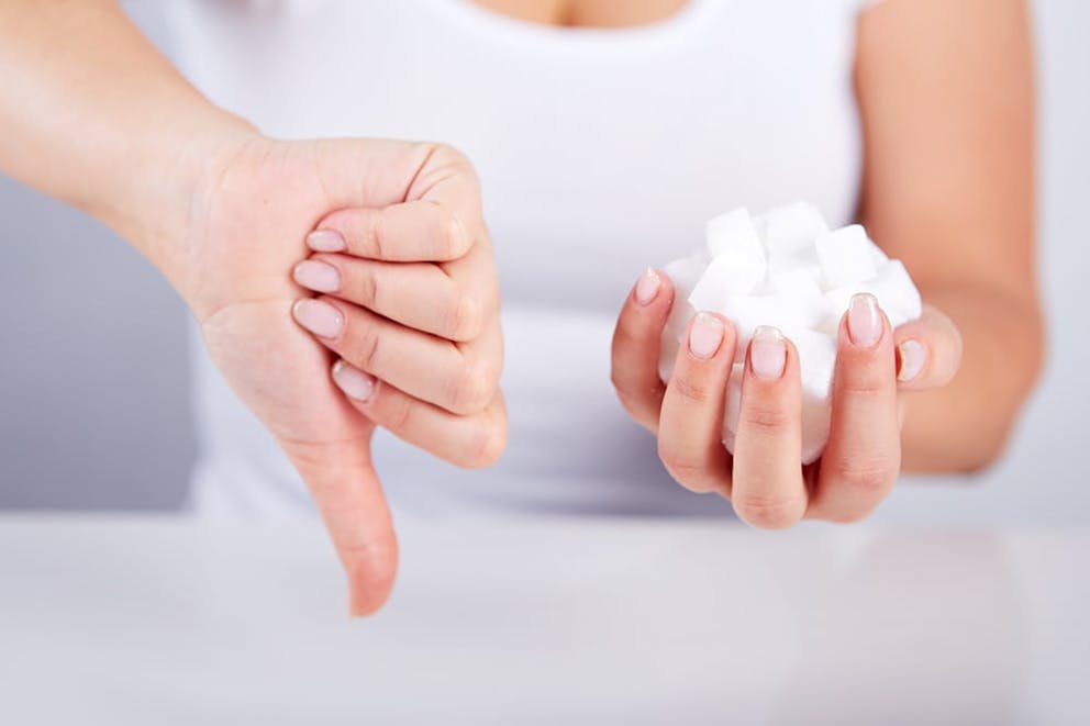 Woman holds handful of sugar cubes and does thumbs down sign, no sugar concept.