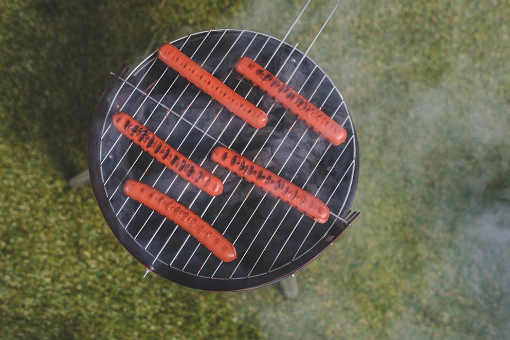Hot dogs cooking on a barbecue in the grass, grill marks top view.