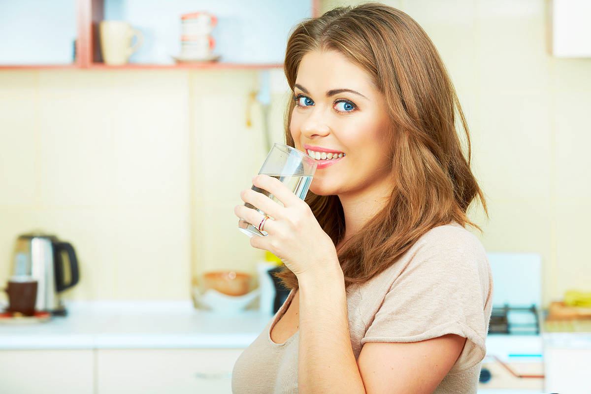 Portrait of happy young woman drinking water against kitchen background | Amazing Health Benefits of Prolonged Fasting | long fasting