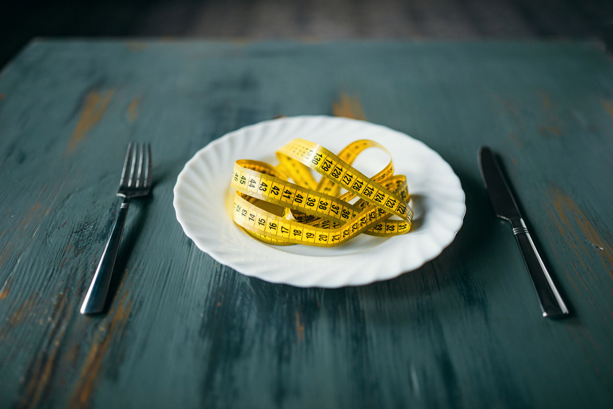 Measuring tape on a plate set with fork and knife, symbolizing weight loss