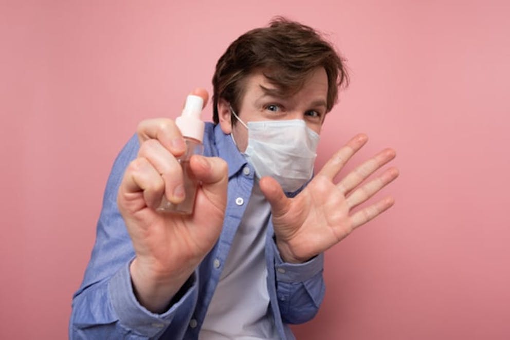 Young man wearing mask looking scared, holding spray bottle of sanitizer, germophobe.