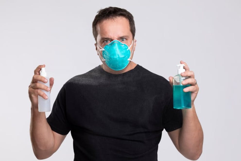 Man in black shirt wearing mask holds disinfectant cleaner and hand sanitizer, killing germs.