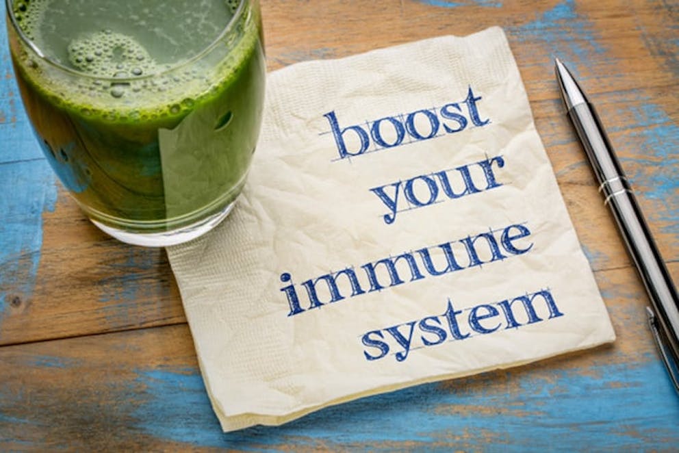 Boost your immune system written on napkin next to pen and glass of healthy green juice.
