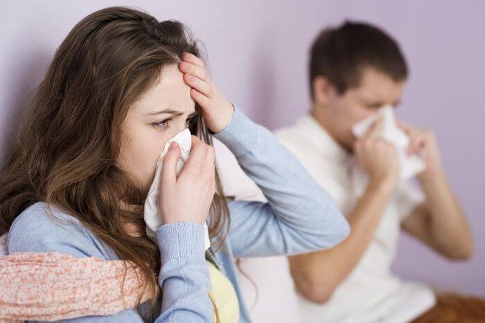 A woman and man both sick in bed blowing their noses.