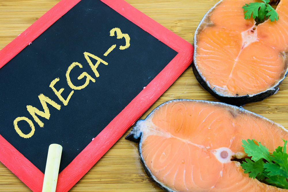 Omega-3 written on a small chalkboard next to two pieces of healthy omega-3- rich salmon.