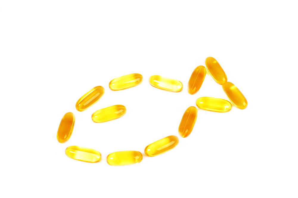 Cod liver oil supplements with omega 3s capsules laid out in the shape of a fish on white background.