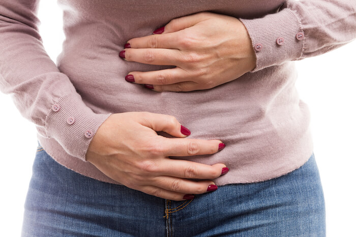 Woman holding stomach with both hands. |  Belly Swelling and Bloating as the Day Progresses