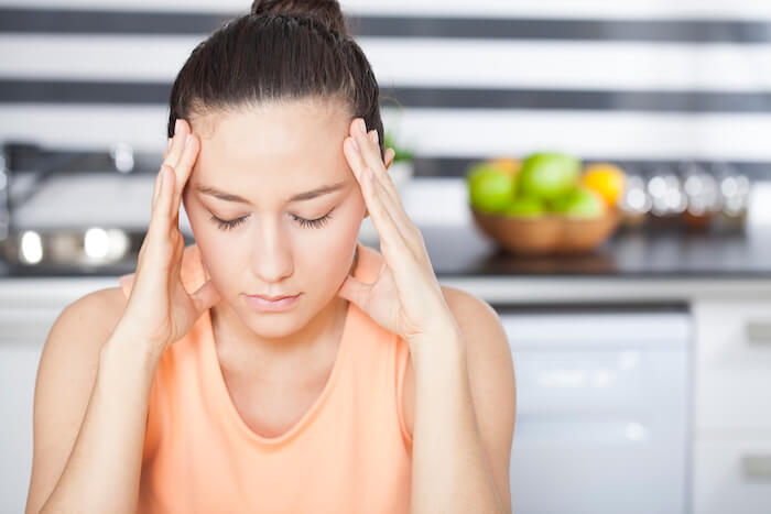 Stressed woman with her eyes closed and hands on her head. |  Belly Swelling and Bloating as the Day Progresses