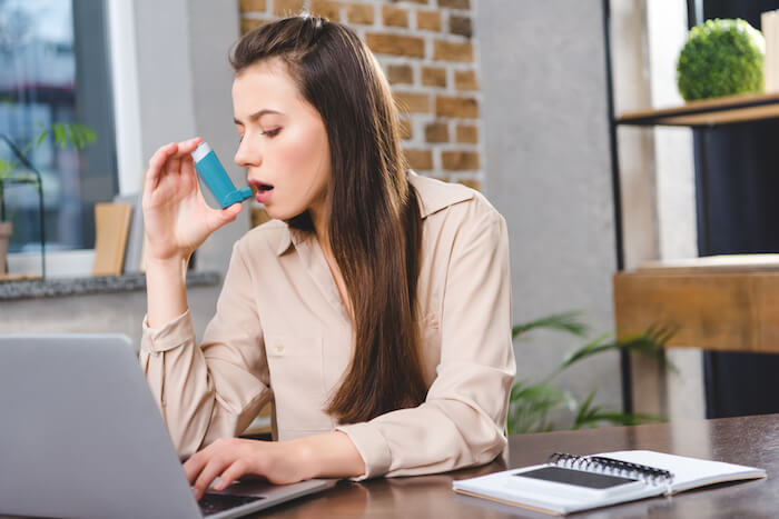 Woman with asthma using an inhaler while working |  Best Asthma Remedies