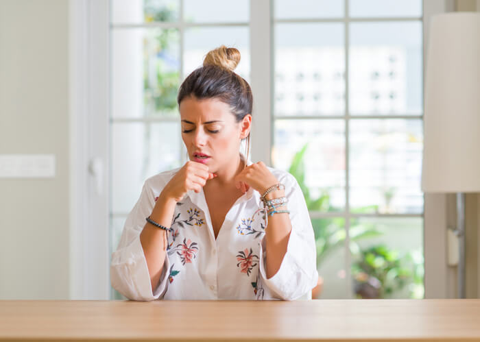 Woman sitting at a table at home coughing |  Best Asthma Remedies