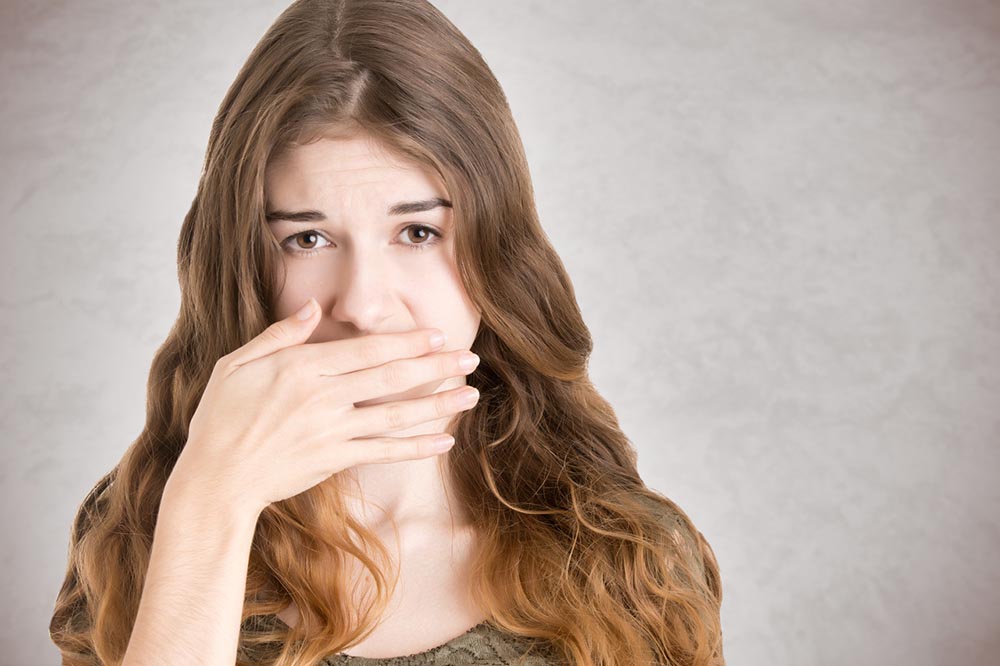 Woman with hand over mouth: A young woman holds her hand over her mouth, covering up bad breath. | Best Bad Breath Remedy