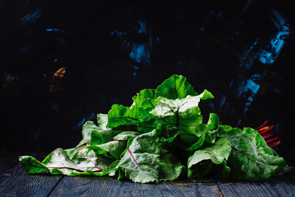 Beet tops on a wooden table against a dark background