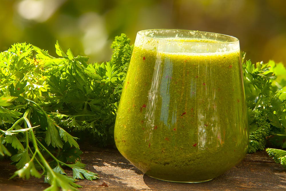 Green liver cleansing shake in a glass with fresh parsley in the background.