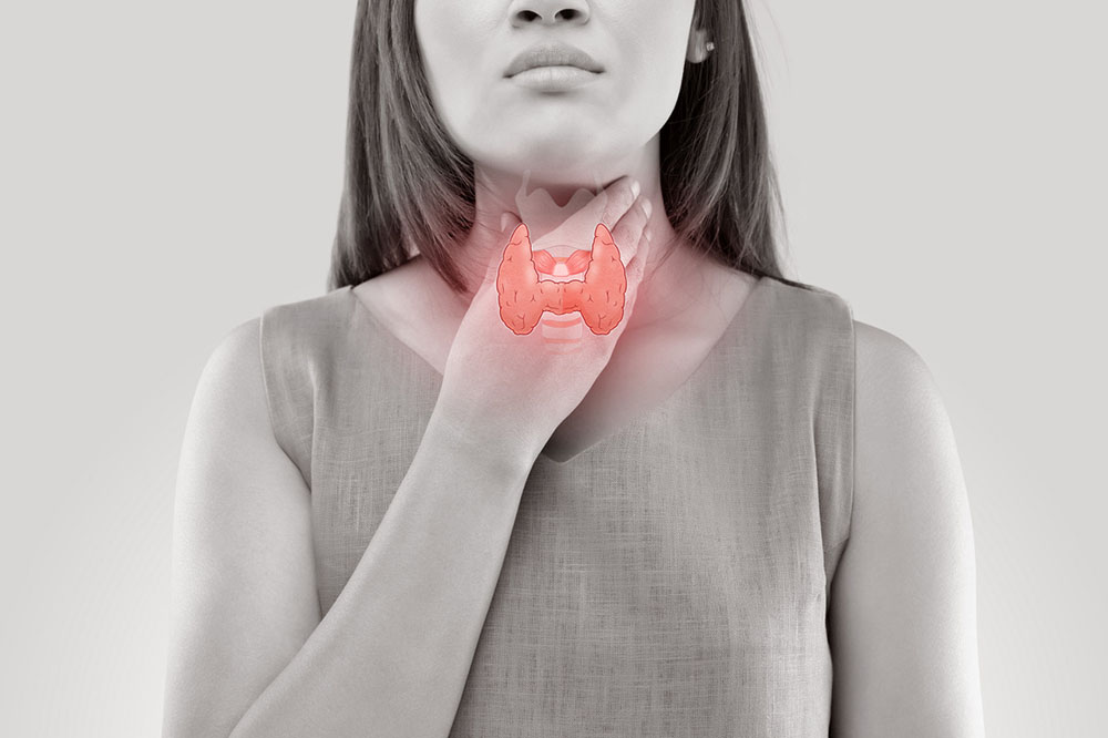 Black and white photo of a woman holding her hand to her neck, with the thyroid gland drawn on top in red.
