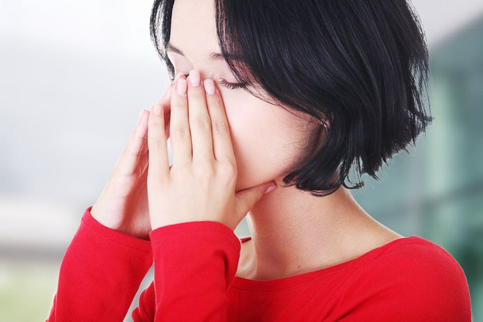 Woman in red shirt with sinus infection and sinus pain, hands on her nose.