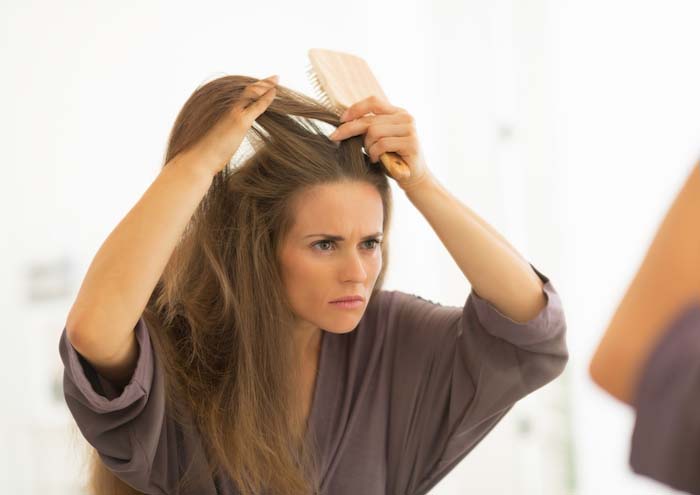 A woman with dandruff looking into a mirror. |  Best Remedies for Dandruff