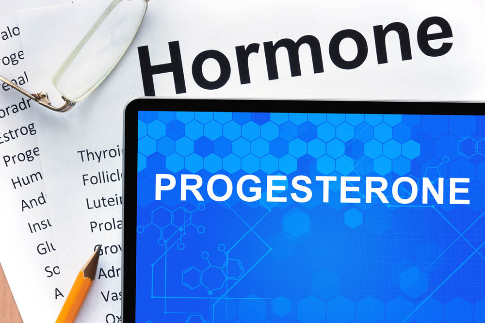 The word progesterone on a screen with drawings of hormones and a list of hormones on paper behind