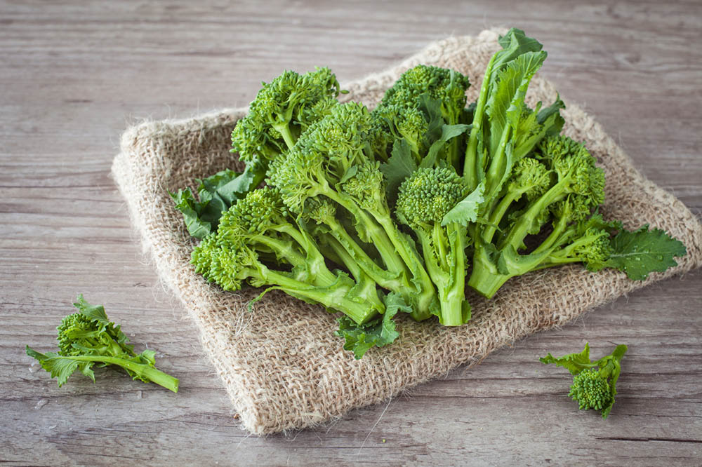 Cut broccoli with leaves sits on burlap sack on a wooden table.