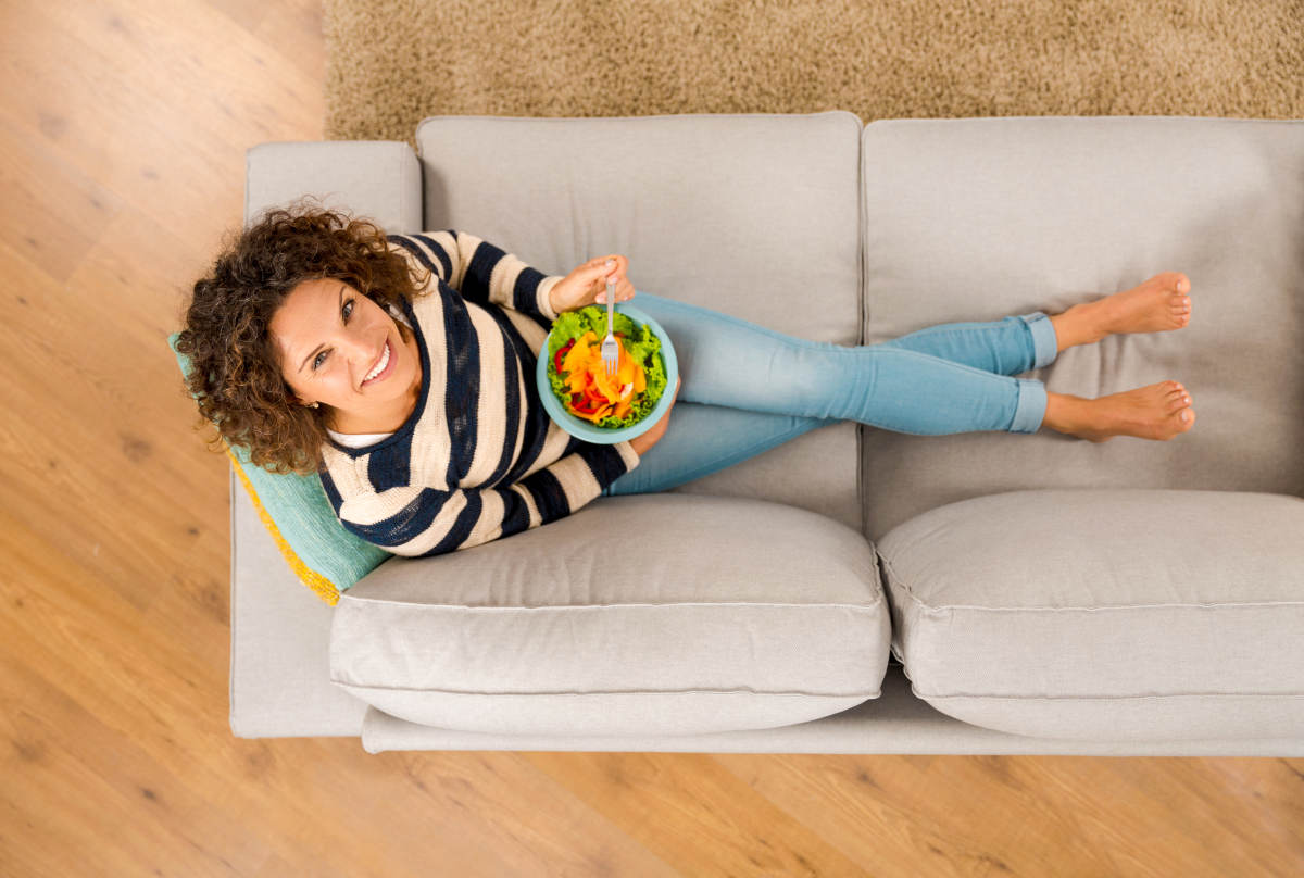 Top view of a beautiful woman on the sofa eating a healthy salad | Calculating Net Carbs on the Ketogenic Diet