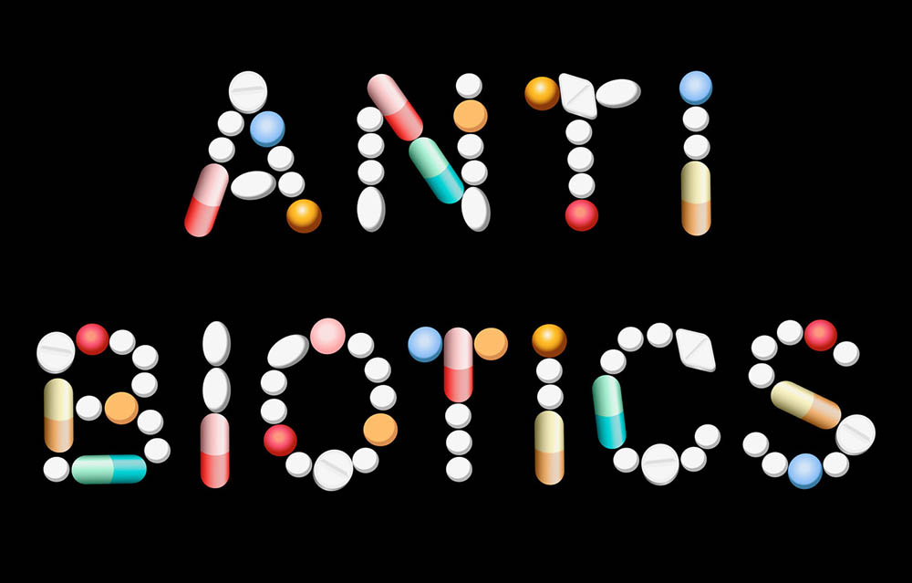 Pills arranged to spell the word antibiotics on a black background | Antibiotics and Weight Gain