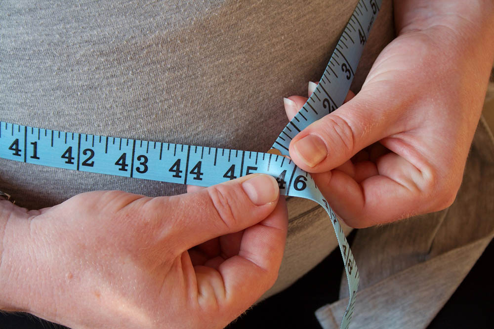 Overweight man holds a blue measuring tape around his belly fat | Antibiotics and Weight Gain