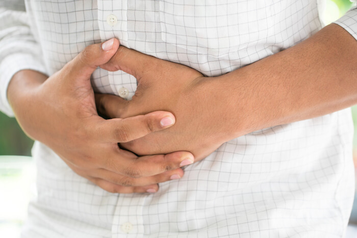 A man with constipation holding stomach with both hands while in pain. |  Constipation Remedies