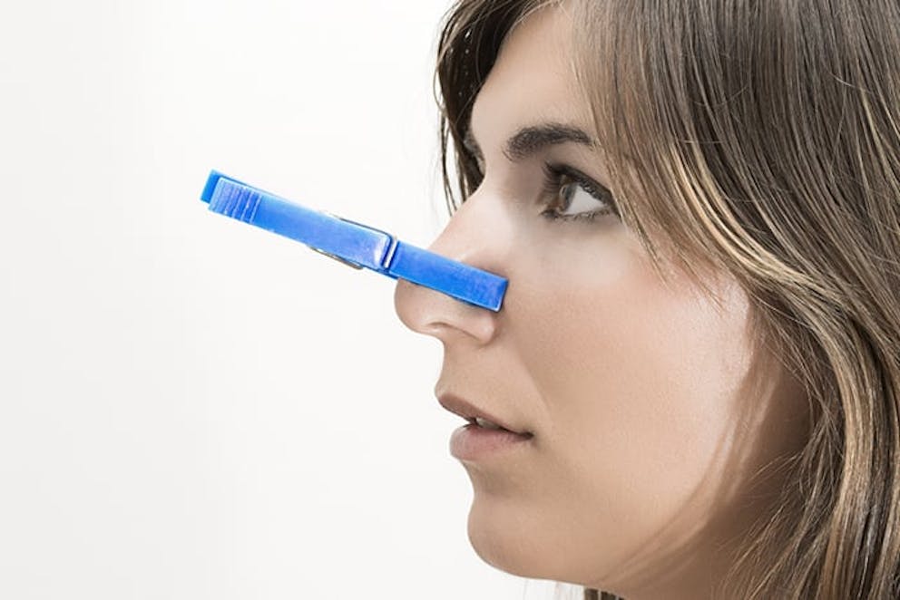 Woman with blue clothespin clipped on her nose, can’t smell, lost sense of smell.