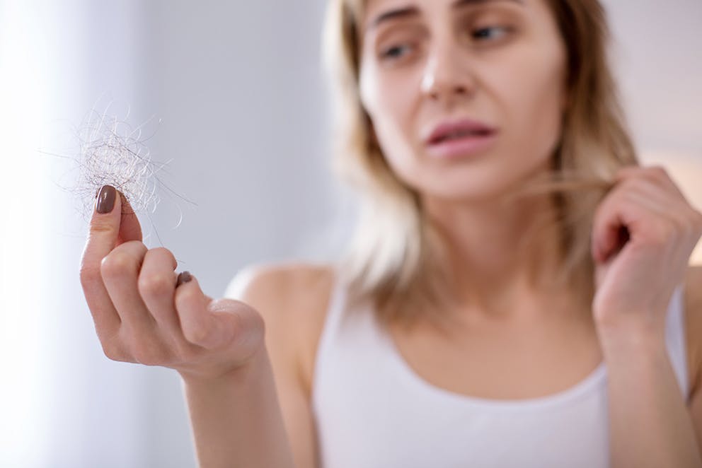 Depressed young woman looking at a clump of her hair that fell out