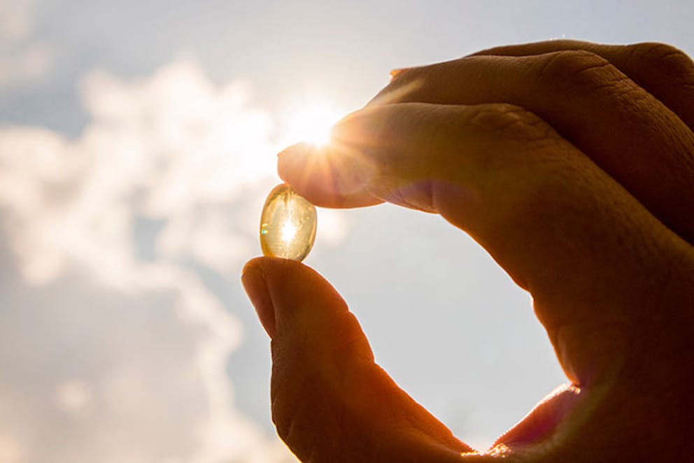 a photo of a capsule of vitamin D being held up to the sky with the sun shining through it