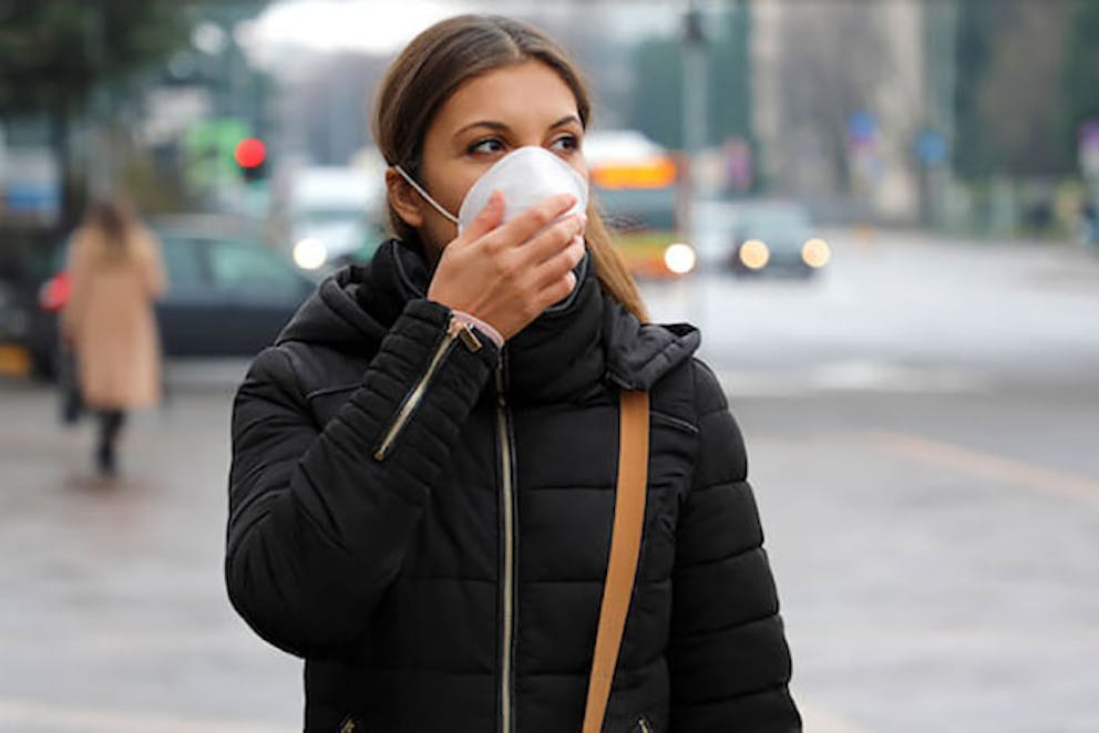 - A woman walking in a city with a mask covering her nose and mouth, protecting her from COVID-19 